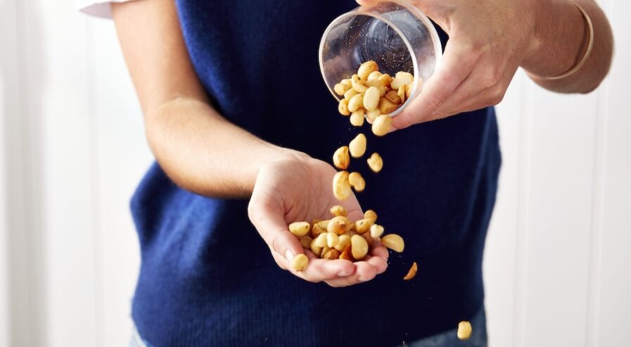 A person tipping macadamia kernel from a jar into their hand
